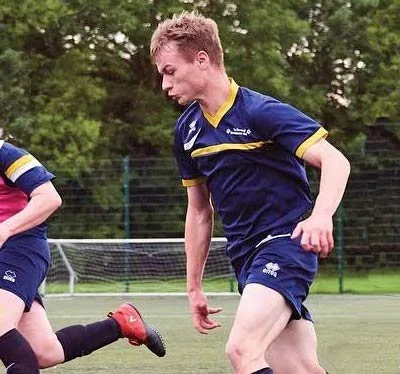 A player in navy and gold kit running with the ball in front of a goal
