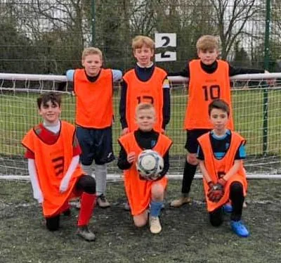 A group of young players in orange bibs with a ball by a goal