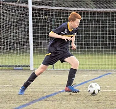 A player in dark kit dribbling a ball in front of a goal